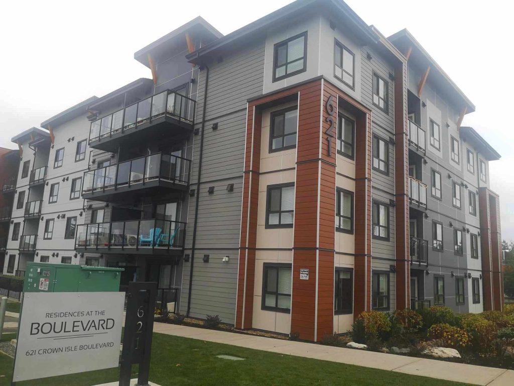 Four-story newer apartment building with balconies on the left side. A sign in the front reads "Residences at the Boulevard. 621 Crown Isle Boulevard.