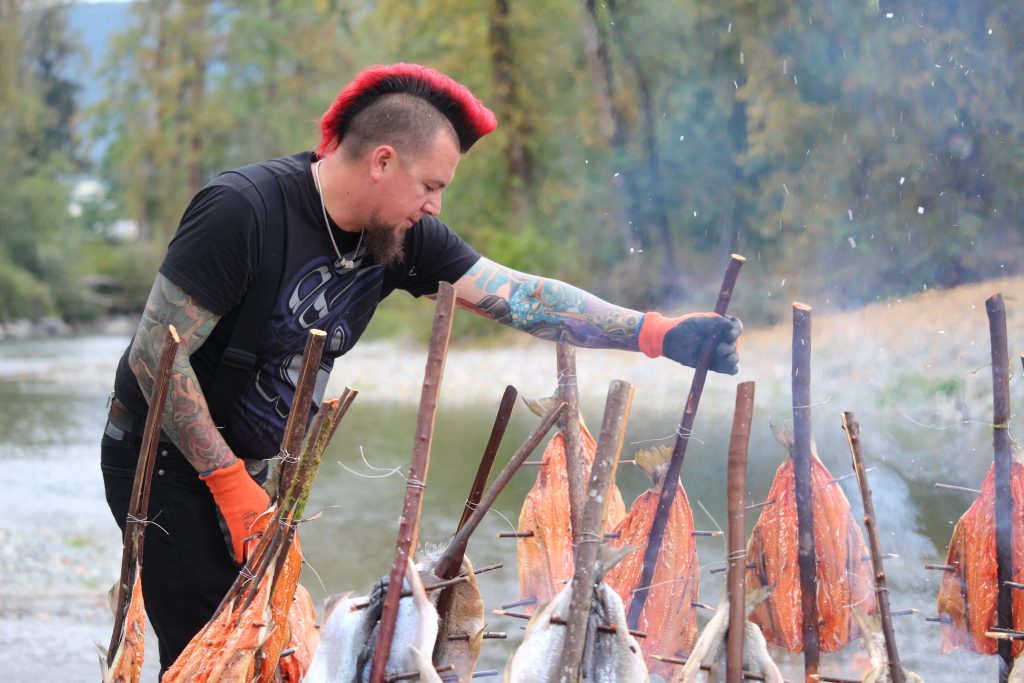 Jared Qwustenuxun Williams tends to a fire and the salmon around it that are speared on long sticks.